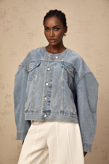 A woman wearing a light blue collarless denim jacket with long sleeves and front pockets