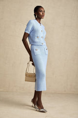 A woman wearing a light blue knitted blouse with short sleeves paired with a matching knee length skirt creating a coordinated outfit set