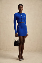 A woman wearing a light blue knitted two piece outfit consisting of a long sleeve top with button details and a matching skirt