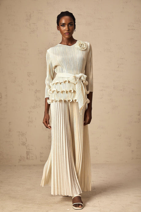 A woman wearing a light colored jumpsuit with floral appliques ruffles and pleats