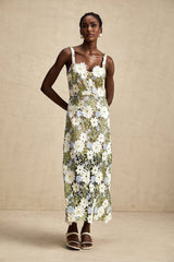 A woman wearing a lightcolored midi dress with floral embroidery and hollowcarved detailing standing in an outdoor setting