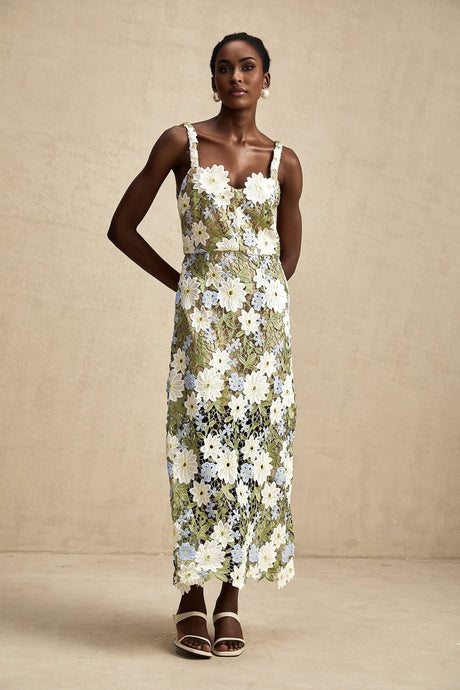 A woman wearing a lightcolored midi dress with floral embroidery and hollowcarved detailing standing in an outdoor setting