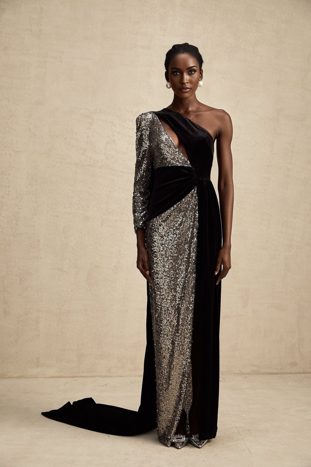A woman wearing a long asymmetrical maxi dress with allover sequin embellishment shimmering in the light The dress features a high slit on one side revealing the leg