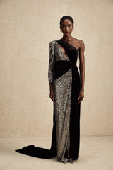A woman wearing a long asymmetrical maxi dress with allover sequin embellishment shimmering in the light The dress features a high slit on one side revealing the leg