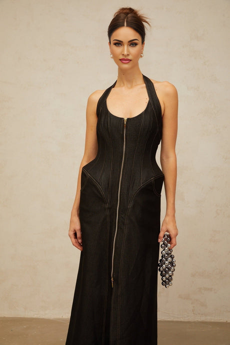 A woman wearing a long black denim maxi dress with a front slit and visible contrast stitching standing against a plain background