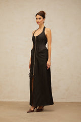 A woman wearing a long black denim maxi dress with a front slit and visible contrast stitching standing against a plain background