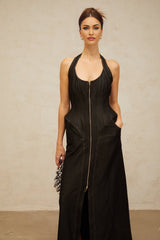 A woman wearing a long black denim maxi dress with a front slit and visible contrast stitching standing in a casual pose