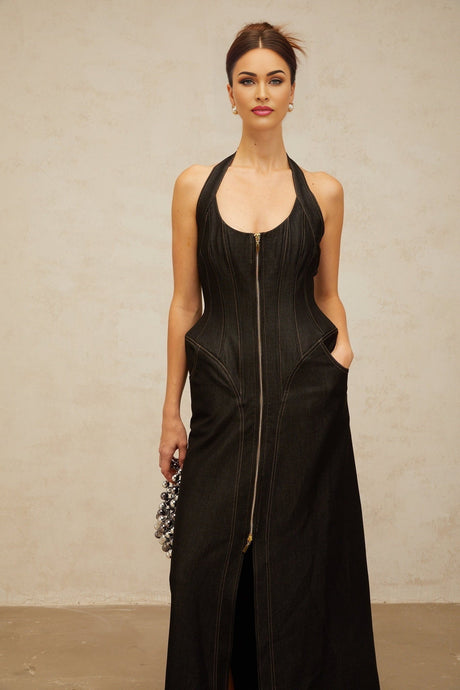 A woman wearing a long black denim maxi dress with a front slit and visible contrast stitching standing in a casual pose