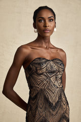 A woman wearing a long black dress with a corset bodice covered in sequins and a sheer mesh skirt