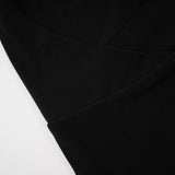 A woman wearing a long black maxi dress with a hood and floral appliques standing against a plain background