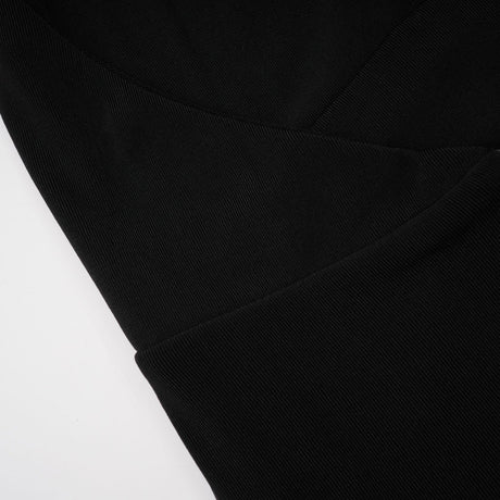 A woman wearing a long black maxi dress with a hood and floral appliques standing against a plain background