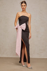A woman wearing a long black offshoulder maxi dress with a large bow detail at the neckline