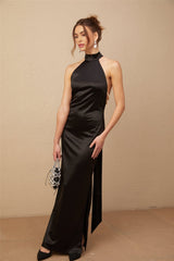 A woman wearing a long black satin maxi dress with a halterneck style and faux pearl embellishments