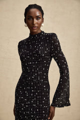 A woman wearing a long black semi sheer maxi dress with embellishments standing in a neutral setting
