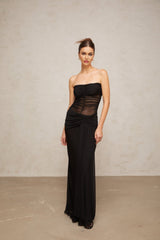 A woman wearing a long black semi sheer pleated tulle maxi dress with a fitted bodice and flowing skirt