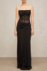 A woman wearing a long black semi sheer pleated tulle maxi dress with a flowing silhouette standing against a plain background