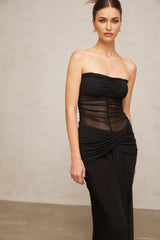 A woman wearing a long black semi sheer pleated tulle maxi dress with a flowing skirt and fitted bodice