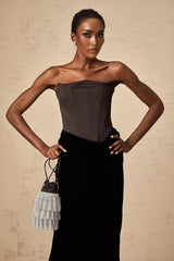 A woman wearing a long black velvet off shoulder maxi dress standing in an elegant pose