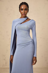 A woman wearing a long blue maxi dress with a diagonal shawl neckline and fitted silhouette