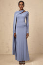A woman wearing a long blue maxi dress with a diagonal shawl neckline and fitted silhouette