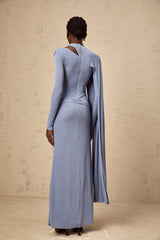 A woman wearing a long blue maxi dress with a fitted silhouette and a diagonal shawl detail across the bodice