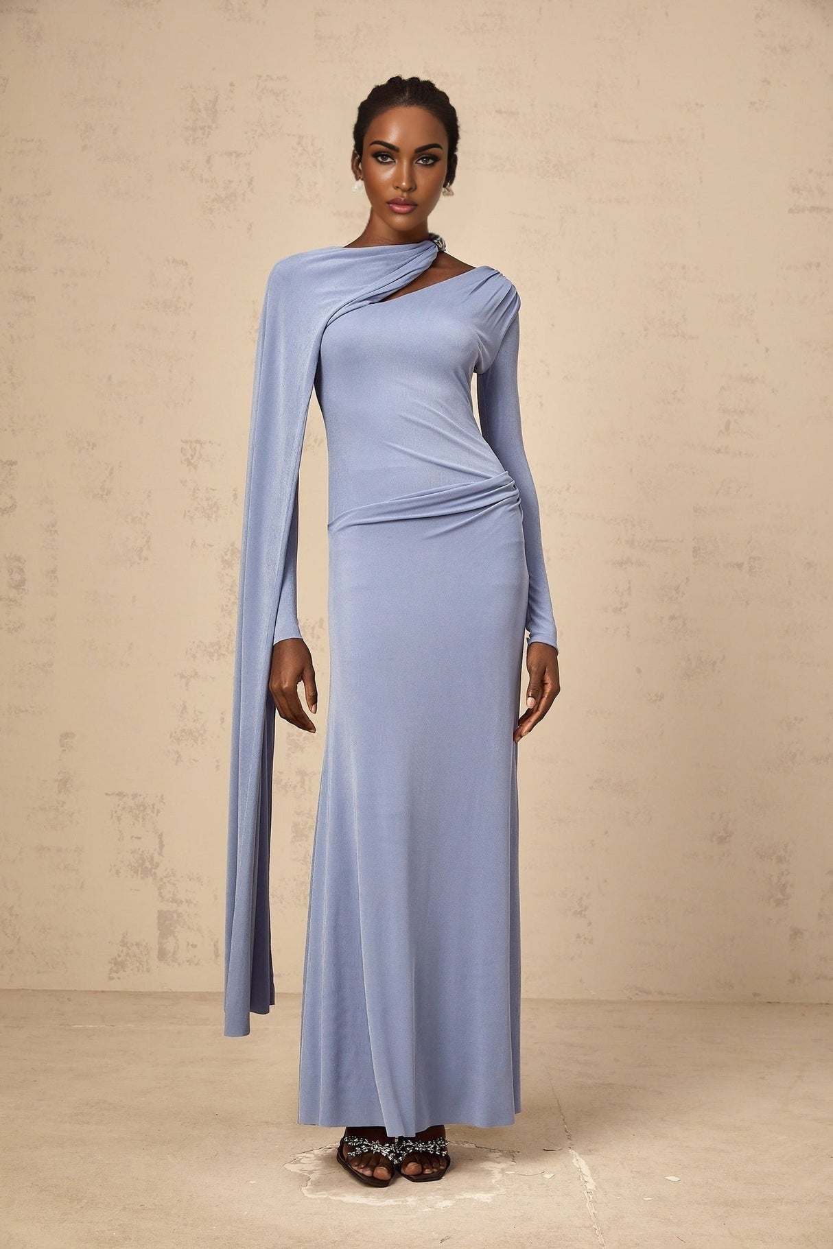 A woman wearing a long blue maxi dress with a fitted silhouette and diagonal shawl neckline