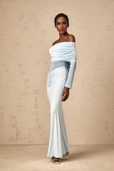 A woman wearing a long blue offshoulder dress with ruched detailing standing against a plain background