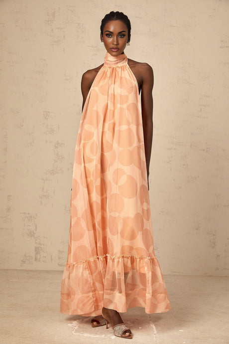 A woman wearing a long coralpink halterneck maxi dress with a pattern print flowing to the floor