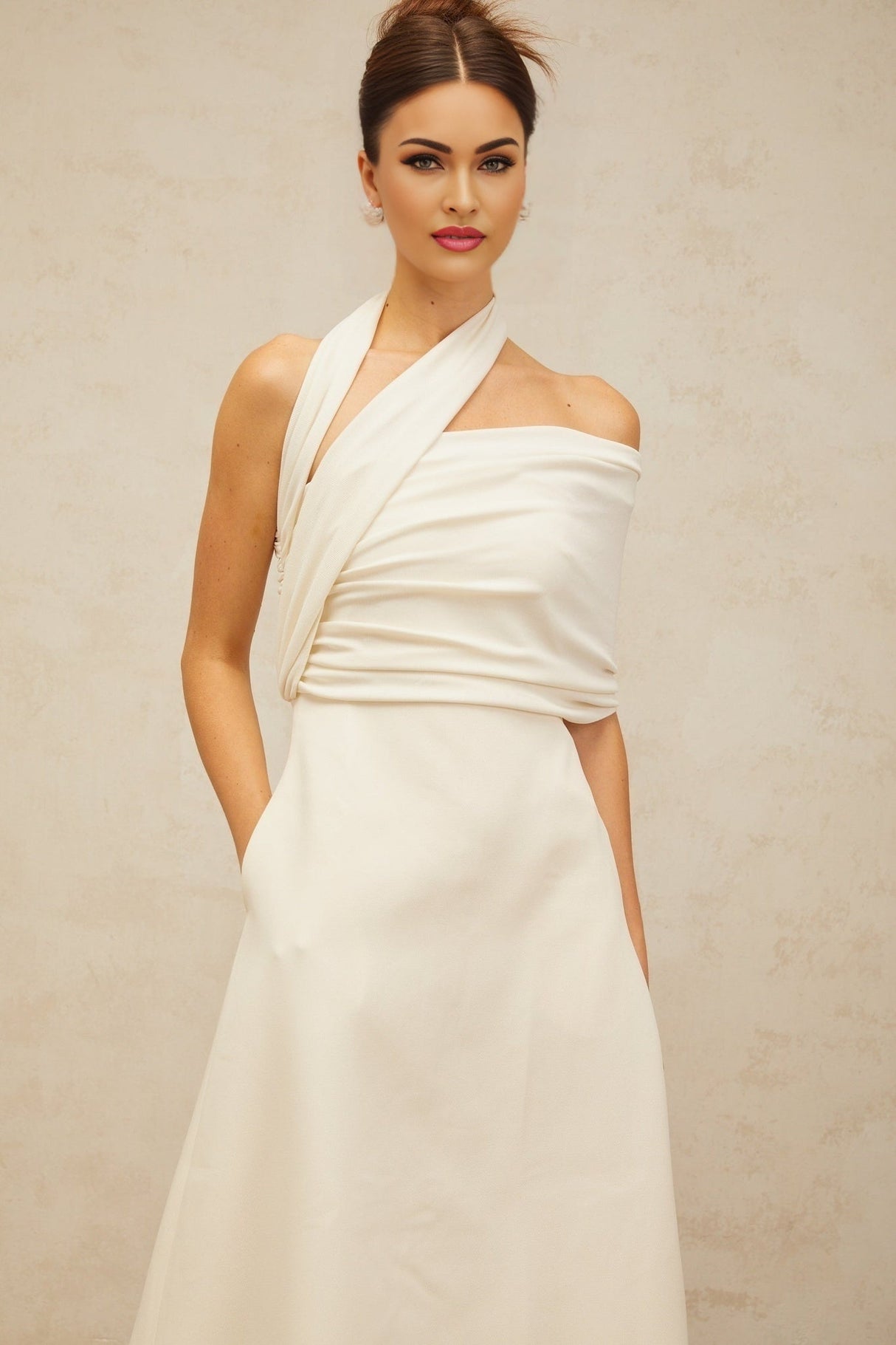A woman wearing a long creamwhite maxi dress with an asymmetric design featuring a high slit and flowing fabric
