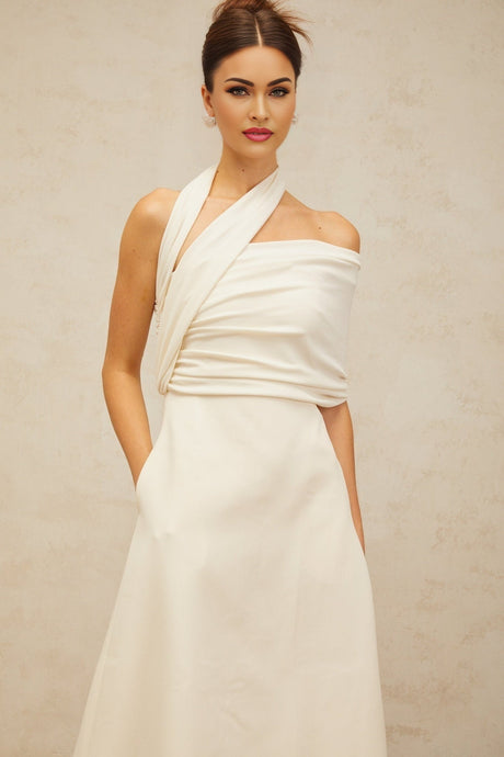 A woman wearing a long creamwhite maxi dress with an asymmetric design featuring a high slit and flowing fabric