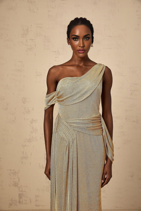 A woman wearing a long flowing gold maxi dress with a gathered waist and ribbon design details