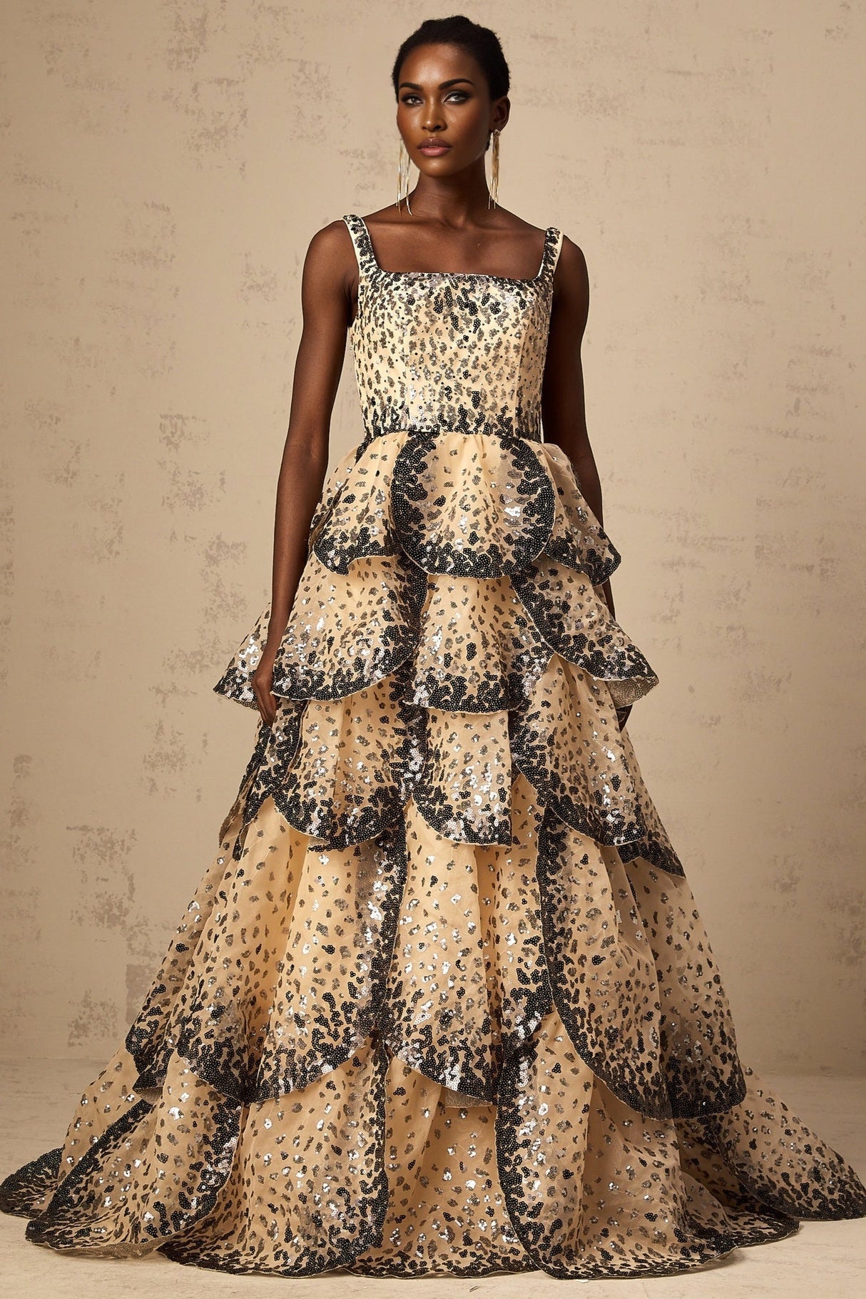 A woman wearing a long flowing maxi dress with tiered layers and shimmering sequin details resembling flower petals