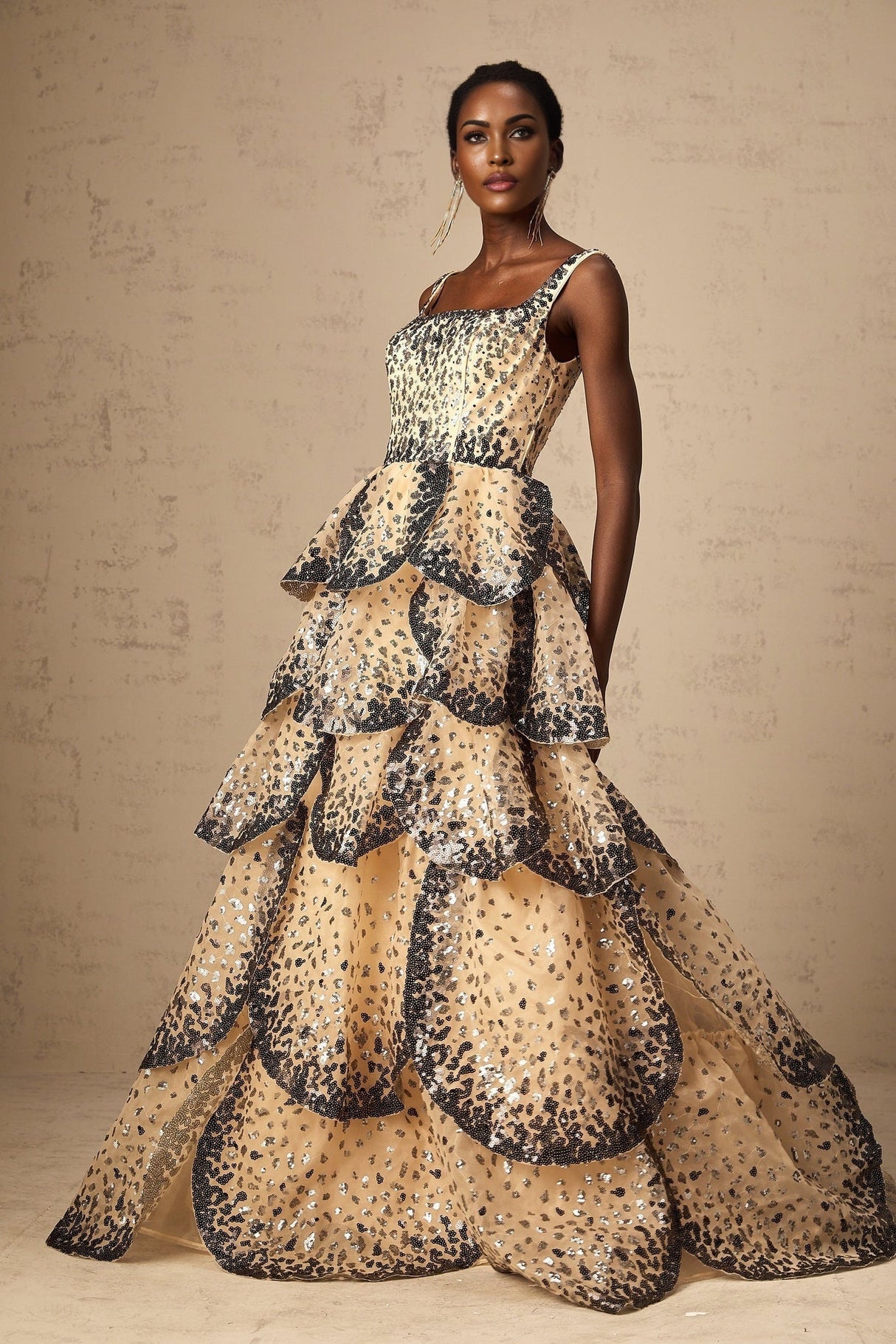 A woman wearing a long flowing maxi dress with tiered layers covered in shimmering sequins resembling delicate flower petals