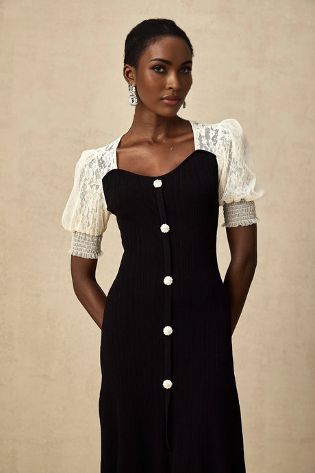 A woman wearing a long knit midi dress with lace trim details along the neckline and hem standing in a relaxed pose against a plain background