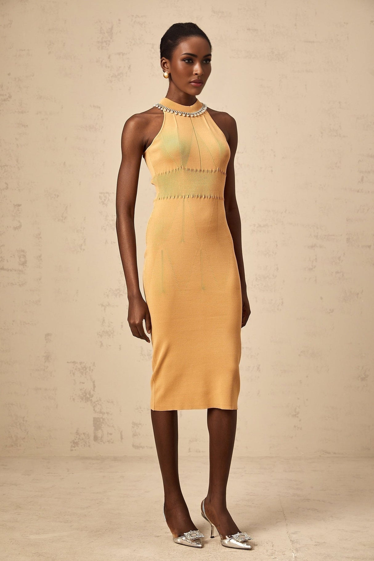 A woman wearing a long knitted dress with faux pearl embellishments throughout the design