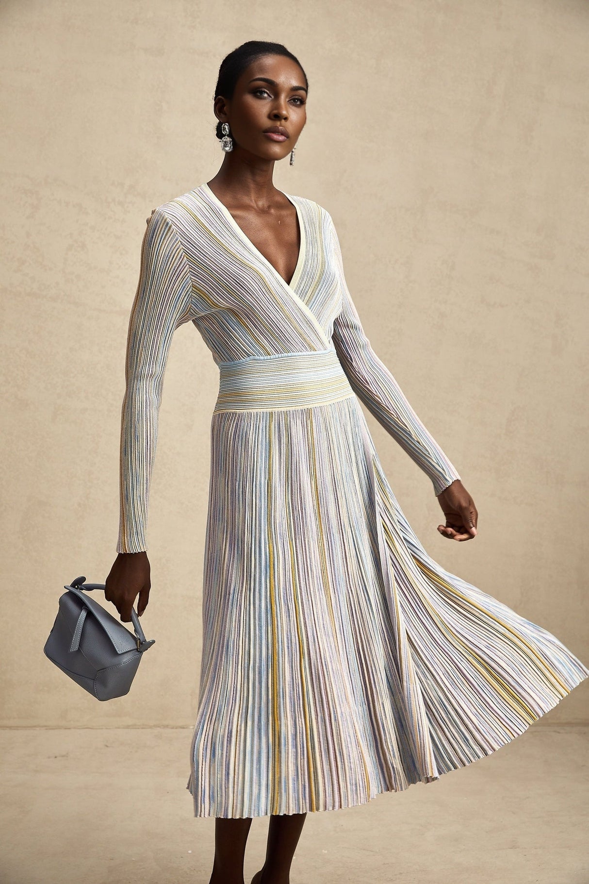 A woman wearing a long knitted midi dress with vertical stripes standing in a casual pose