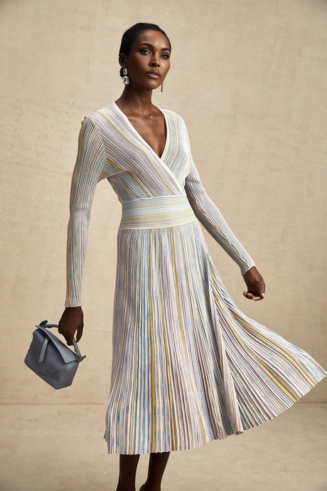 A woman wearing a long knitted midi dress with vertical stripes standing in a casual pose
