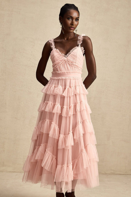 A woman wearing a long light colored maxi dress with multiple layers of ruffled tulle fabric creating a flowing and romantic silhouette