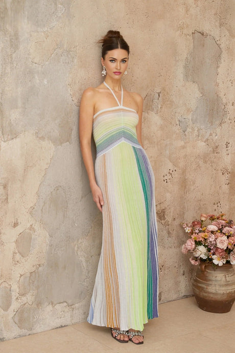 A woman wearing a long metallic knit maxi dress with a backless design standing in a relaxed pose