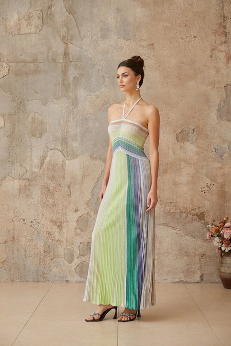 A woman wearing a long metallic knit maxi dress with a backless design standing in a relaxed pose