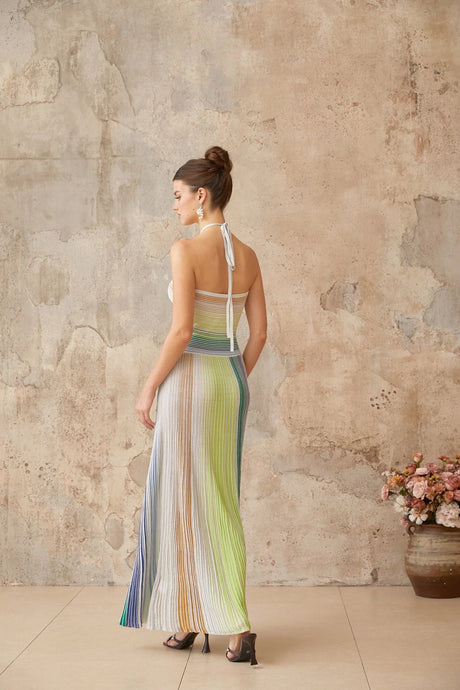 A woman wearing a long metallic knit maxi dress with a backless design standing in a stylish pose