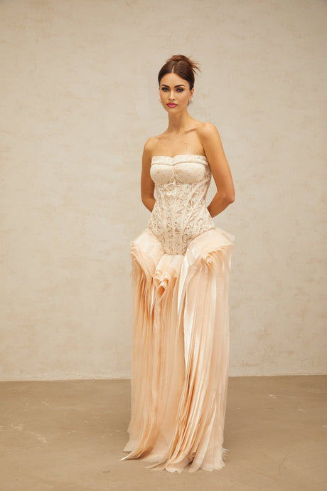 A woman wearing a long neutral colored maxi dress with lace details and corset style bodice layered over a full skirt