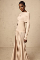 A woman wearing a long neutralcolored maxi dress with ribbon design details and elegant draping