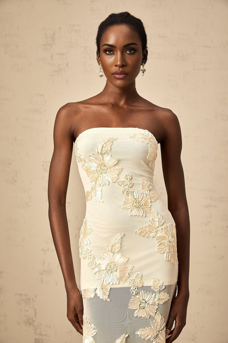 A woman wearing a long offshoulder maxi dress in neutral colors with embroidered details standing in a relaxed pose