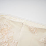 A woman wearing a long offshoulder maxi dress in neutral tones with embroidered details standing in a relaxed pose