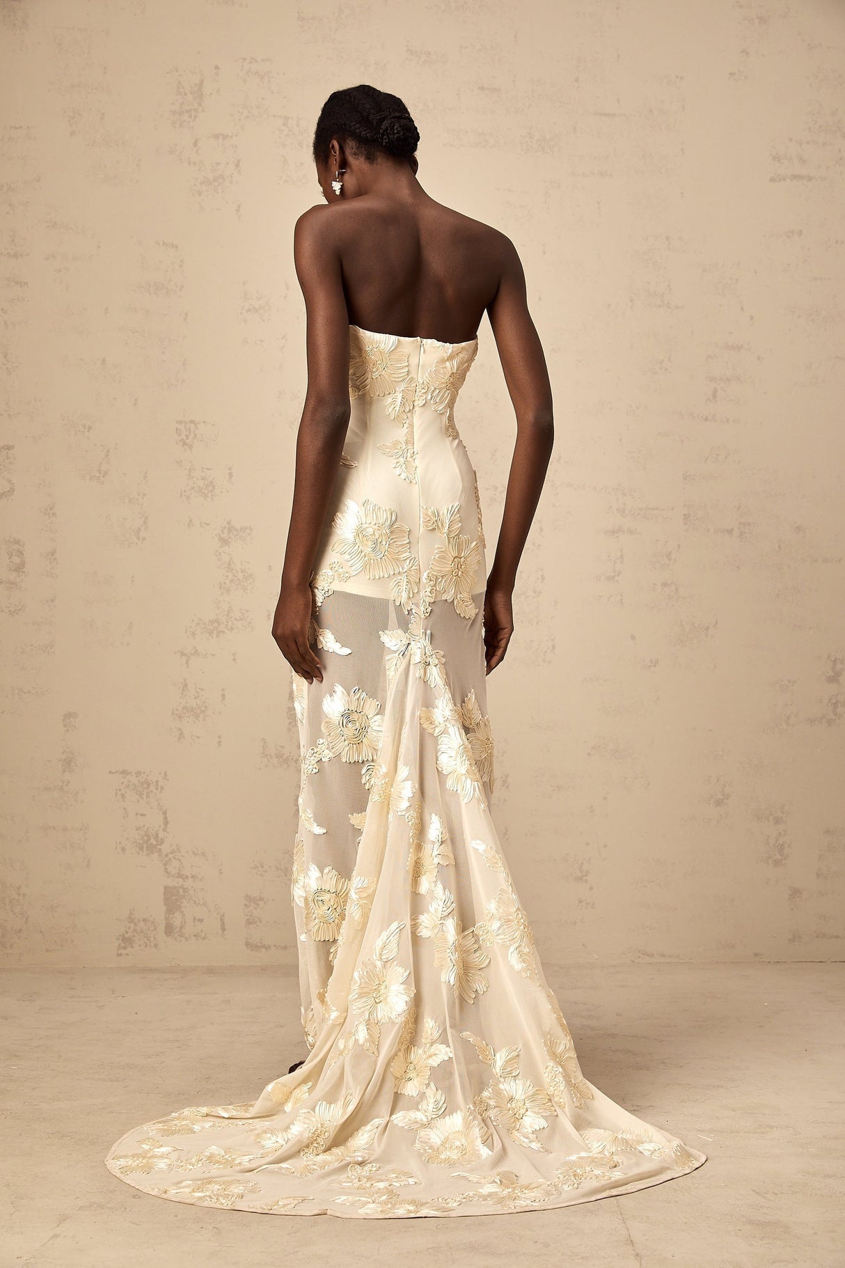 A woman wearing a long offshoulder maxi dress in neutral tones with embroidery details