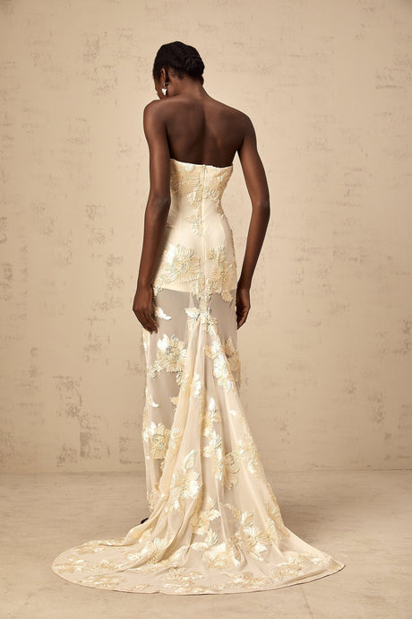 A woman wearing a long offshoulder maxi dress in neutral tones with embroidery details