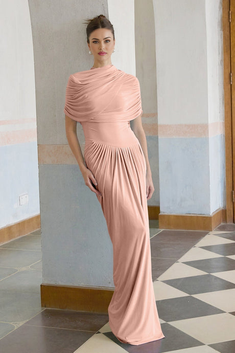 A woman wearing a long pink dress with an asymmetric neckline and pleated skirt standing in a neutral background