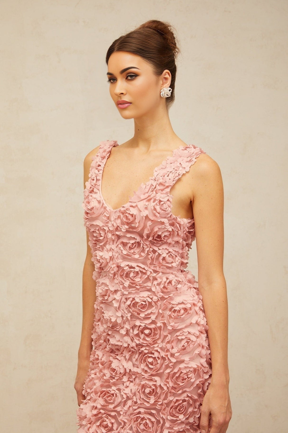 A woman wearing a long pink floral dress with a V neckline and faux flower pattern standing in a neutral background