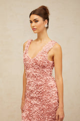 A woman wearing a long pink floral dress with a V neckline and faux flower pattern standing in a neutral background